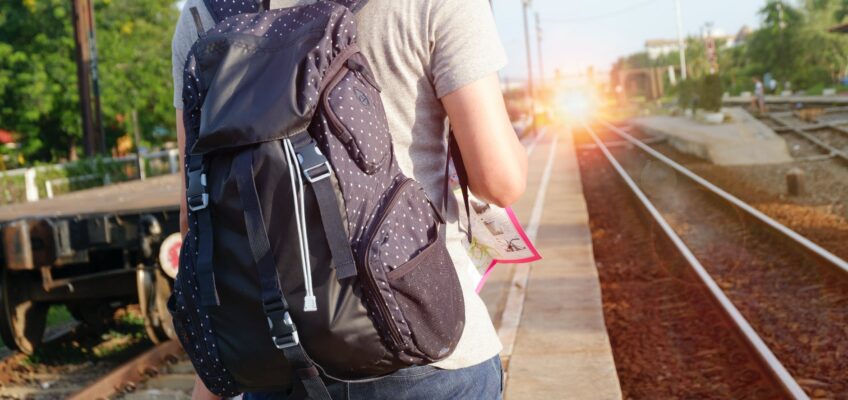 person in grey top with backpack waiting for train